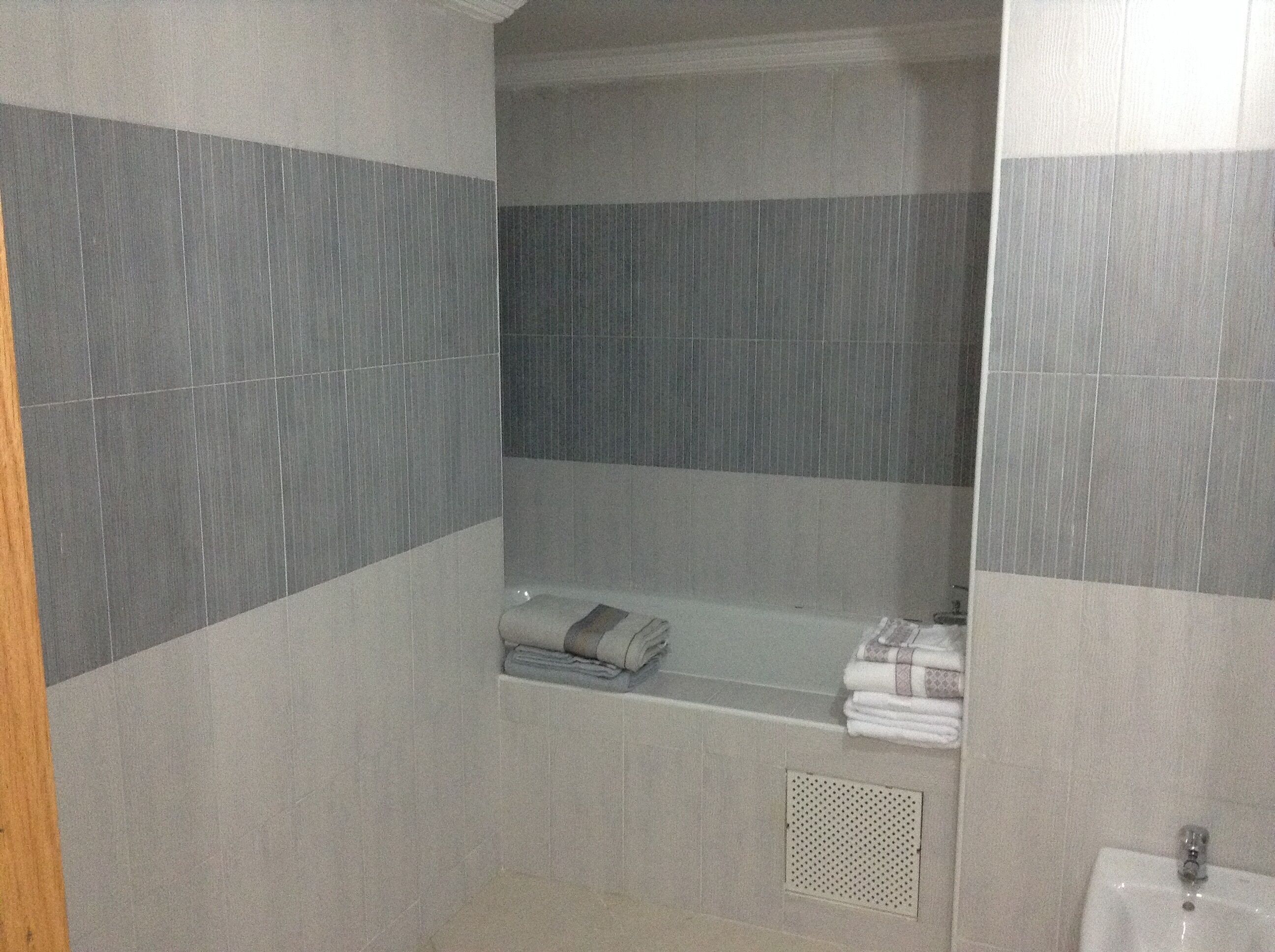 Un baño con paredes de baldosas grises, una bañera, un inodoro y un lavamanos.
