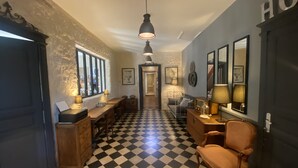 A hallway with a checkered floor, a wooden bench, a table with lamps, and a chair.