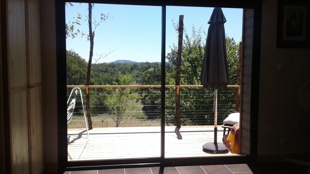 A room with a large sliding glass door leading to an outdoor deck. The deck has a metal railing and a single umbrella. - Promo end of August 25% 3 bedroom cottage of 85m2 with south facing terrace of 60m2  (Saint-Cyr-La-Roche)
