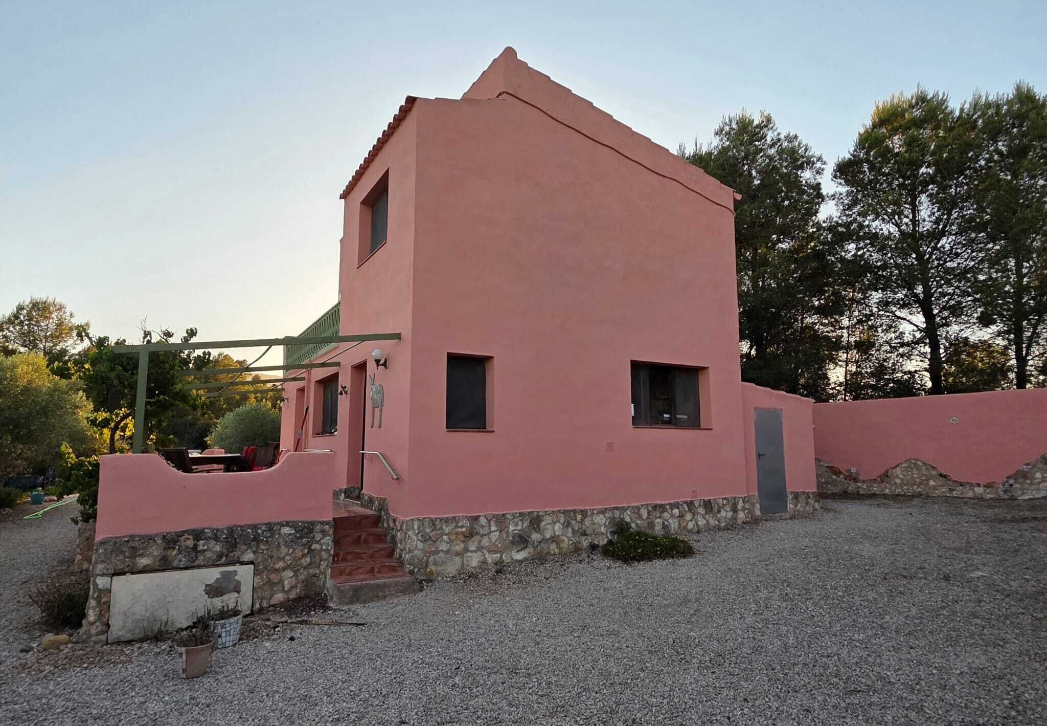 A pink building with a stone foundation, a small porch, and a gravel driveway.
