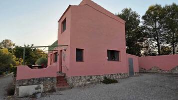 A pink building with a stone foundation, a small porch, and a gravel driveway.