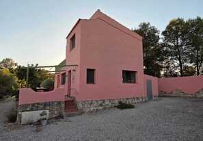 A pink building with a stone foundation, a small porch, and a gravel driveway. - Wonderful country house with private pool (El Perelló)