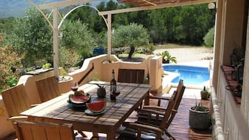 A covered outdoor dining area with a pool in the background.
