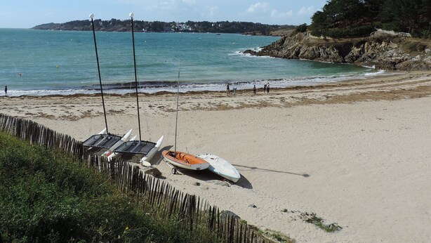Une plage bordée d’une rangée de bateaux et d’une clôture en bois.