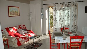 Un coin repas avec une table dressée pour deux personnes, une chaise rouge et un canapé recouvert d’un plaid rouge et blanc.