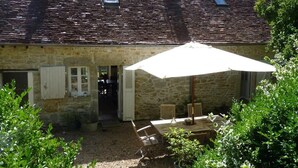 A stone building with a tiled roof, a patio with a table and chairs, and a small window. - Adorable country house in the heart of a hamlet overlooking the valley (Authiou)