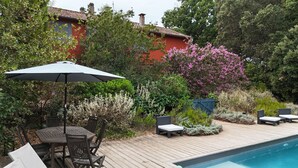 Une terrasse en bois avec une piscine, du mobilier d’extérieur et une végétation luxuriante.