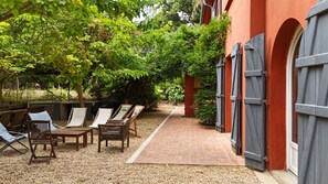 Un patio con mobiliario exterior, un sendero de grava y un edificio rojo con contraventanas grises.