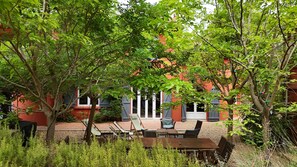 An outdoor seating area with tables and chairs, surrounded by trees and a red building with windows. - Provençal property with swimming pool and pétanque court in a wooded area (Six-Fours-Les-Plages)