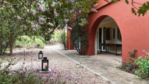 Un chemin menant à un bâtiment doté d’une entrée en arc de cercle, entouré d’arbres et de fleurs violettes.