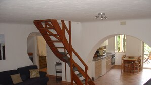 Ein Wohnzimmer mit einer Holztreppe, einem Essbereich mit Tisch und Stühlen sowie einer durch einen Bogen sichtbaren Küche.