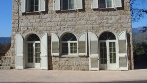 Ein Gebäude aus Stein mit zahlreichen Fenstern und Eingängen, das traditionelle Architektur mit Fensterläden aufweist.