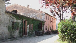 A rustic building with a gravel driveway, arched windows, and a table with chairs outside. - La Corte Charming Tuscany Villa (Siena)