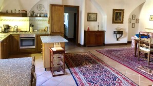 A spacious kitchen with wooden cabinets, a granite countertop, and a built-in oven. There are two rugs on the floor, a dining table with chairs, and a wooden bench. - La Corte Charming Tuscany Villa (Siena)