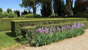 A formal garden with neatly trimmed hedges, a gravel path, and purple flowers. - La Corte Charming Tuscany Villa (Siena)