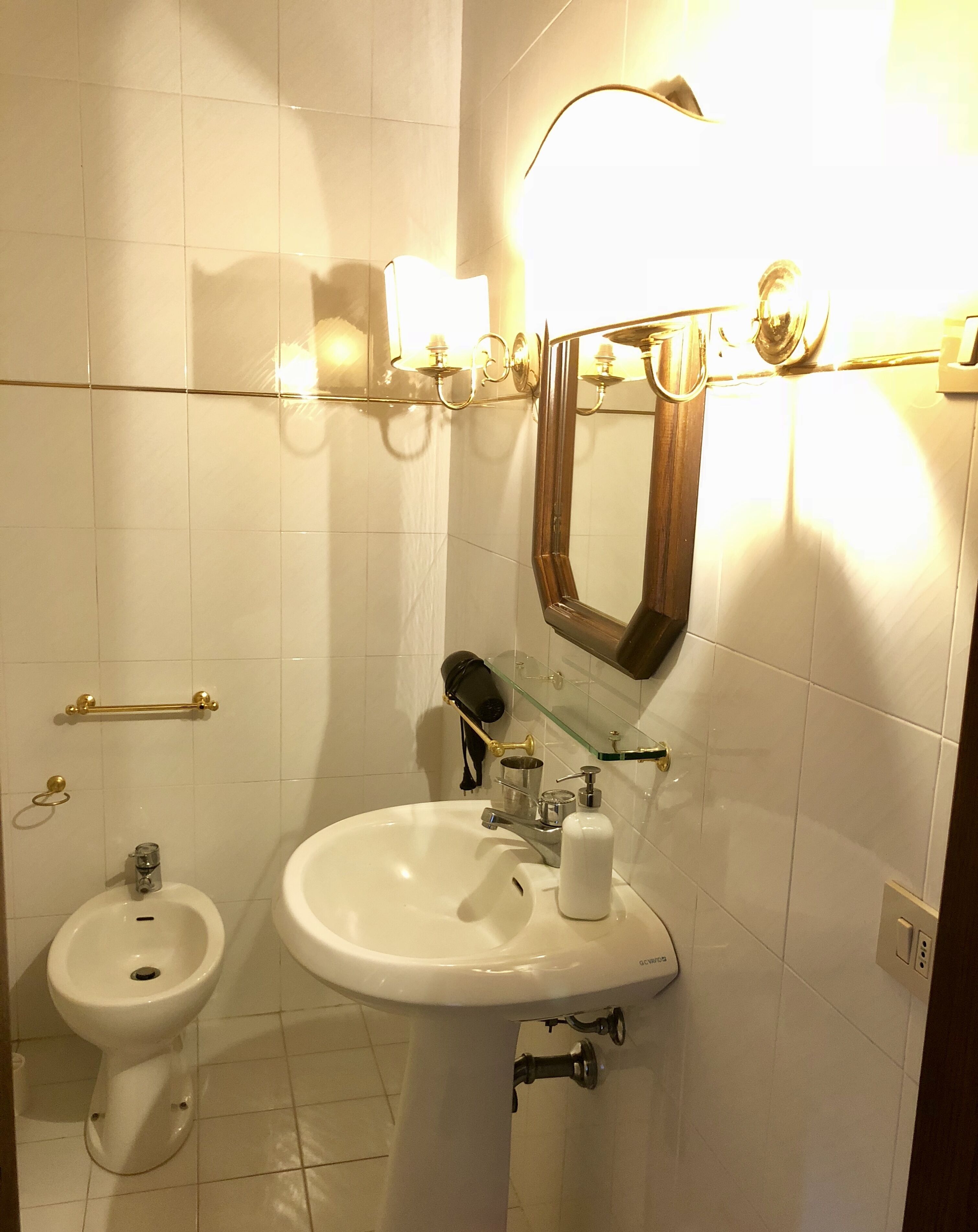 Un bany amb un vàter blanc, un bidet, un mirall i llums penjades a la paret.