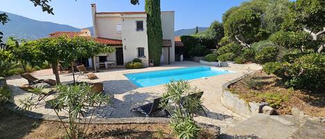 A pool area with lounge chairs, a stone patio, and a building with a tiled roof.