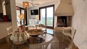 Un comedor con una mesa redonda de vidrio, sillas blancas, una cesta tejida y un ventilador de techo.