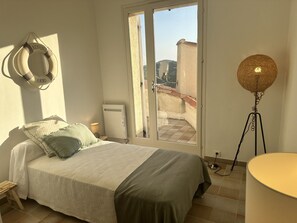 A bedroom with a bed, a nightstand, a lamp, a radiator, and a view through a sliding door to an outdoor balcony. - 900m from beach and stores, air-conditioned villa, swimming pool. Sea and harbor view (Cavalaire-Sur-Mer)