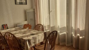 A dining area with a table set for four, wooden chairs, a ceiling fan, and a window with sheer curtains. - Lelex Monts-Jura to rent studio facing south and resort center  (Lélex)