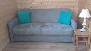 A grey sofa with teal cushions, a small wooden table, and a white lamp with a decorative shade. - Lelex Monts-Jura to rent studio facing south and resort center  (Lélex)