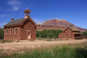 A rustic two-story building with a bell tower, surrounded by a dry, grassy landscape and mountains in the background.