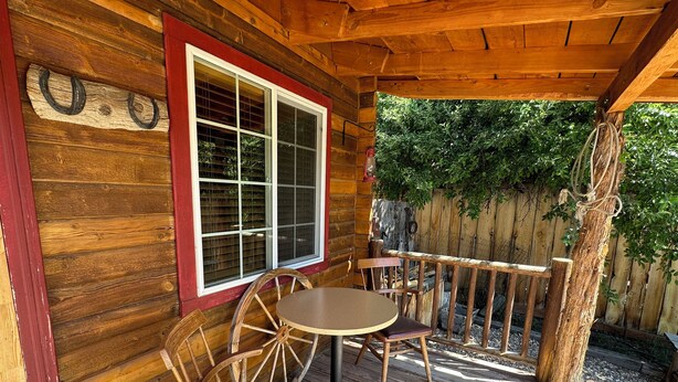 A wooden cabin with a porch, a round table, two chairs, and a window with a red frame. - Relax In Southern Utah's Color Country! (MOUNT CARMEL)
