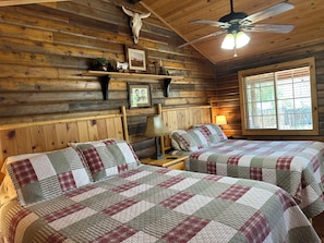 A cabin with two beds, wooden walls, a ceiling fan, and a window with blinds.