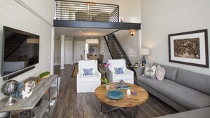 A spacious living area with a high ceiling, a staircase, a grey sofa, white armchairs, a wooden coffee table, and a flat-screen TV. - Spectacular Seabrook Island Villa, unlike any other, includes Club access (Johns Island)