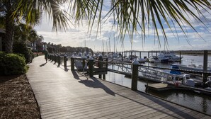 A wooden boardwalk leading to a marina with boats docked, surrounded by greenery and palm trees. - Spectacular Seabrook Island Villa, unlike any other, includes Club access (Johns Island)