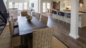 A spacious dining area with a long wooden table and wicker chairs, a kitchen with modern appliances, and a view of the outdoors through large windows. - Spectacular Seabrook Island Villa, unlike any other, includes Club access (Johns Island)
