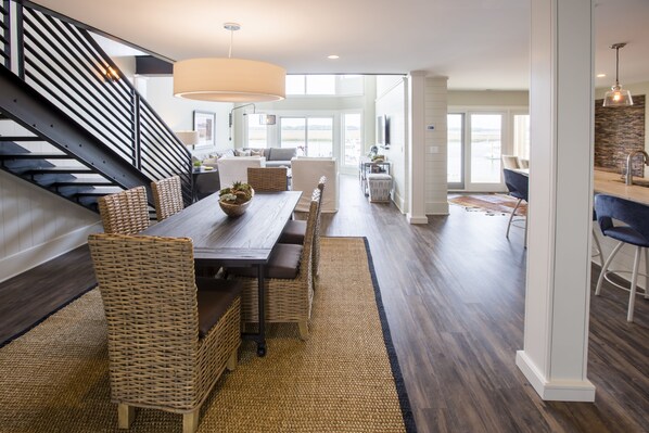 A spacious living area with a large wooden dining table, wicker chairs, and a modern staircase.