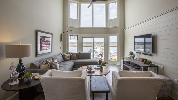 A spacious living room with a large window, a ceiling fan, a sofa, a coffee table, and a TV mounted on the wall. - Spectacular Seabrook Island Villa, unlike any other, includes Club access (Johns Island)