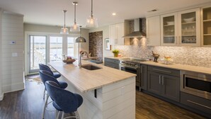 A modern kitchen with a central island, bar stools, stainless steel appliances, and a view to the outside. - Spectacular Seabrook Island Villa, unlike any other, includes Club access (Johns Island)