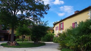 A yellow building with red shutters, a paved driveway, and surrounding greenery. - Beautiful house of 315 m² in a 4000 m² park with swimming pool 3 minutes from Périgueux (Champcevinel)