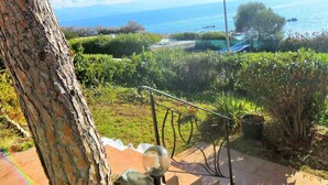 A view of a coastal area with a clear sky, a pathway leading to a body of water, and a boat docked near the shore. - House with garden beach Scudo (Ajaccio)