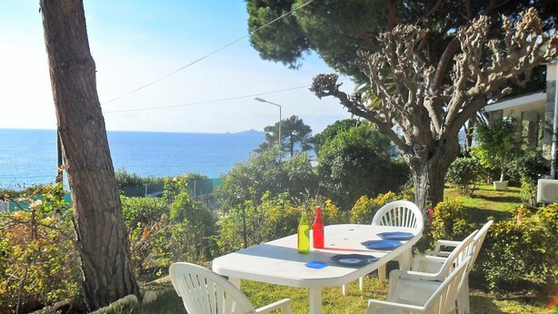 A table set outdoors with chairs, a view of the sea, and a tree in the background. - House with garden beach Scudo (Ajaccio)