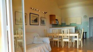 A cozy living room with a white sofa, wooden dining table, and chairs. There is a kitchen area with cabinets and a microwave. - House with garden beach Scudo (Ajaccio)