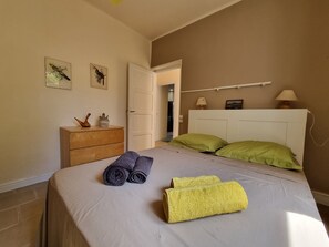 A bedroom with a bed, two pillows, a nightstand, a dresser, and two wall-mounted lamps.