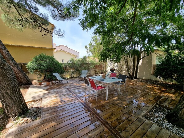 A wooden deck with a table and chairs, surrounded by trees and a building.