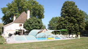 Una casa con piscina, camas de jardín cubiertas y mobiliario de exterior.