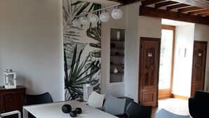 Un comedor con una mesa blanca, sillas negras y blancas, un bol negro y una pared con un mural de plantas.