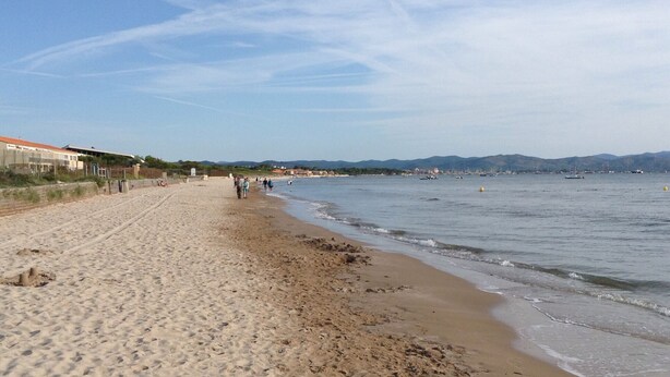 A sandy beach with a few people walking along the shore, a clear sky, and distant mountains. - holiday apartment seaside comfort air-conditioned  (Hyères)