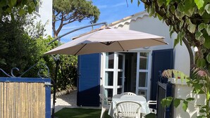 A patio with a table and chairs, a covered umbrella, and a view of a house with a blue door. - holiday apartment seaside comfort air-conditioned  (Hyères)