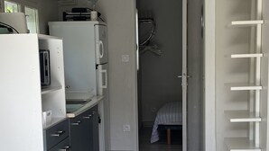 A modern kitchen with a refrigerator, microwave, and kettle. There is a hallway leading to a bedroom with a bed and a hanging rack. - holiday apartment seaside comfort air-conditioned  (Hyères)