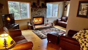 A cozy living room with leather sofas, a fireplace, a television, and a large window. - ~ Cozy Creek Side Cabin ~ Nature ~ Peaceful ~ Relax ~Family!  (Hill City)