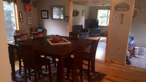 A dining area with a wooden table and chairs, a rug, and a television in the background. - ~ Cozy Creek Side Cabin ~ Nature ~ Peaceful ~ Relax ~Family!  (Hill City)