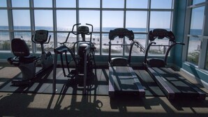 Uma academia com equipamentos de exercícios e amplas janelas com vista para uma praia.
