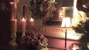 Ein Zimmer mit Spiegel, Kerzen, einem Weihnachtsbaum und einer Blumenkomposition auf einer Holzkombie.