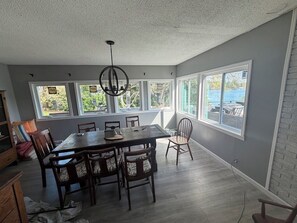 A dining area with a large table and chairs, large windows, and a view of the outdoors.